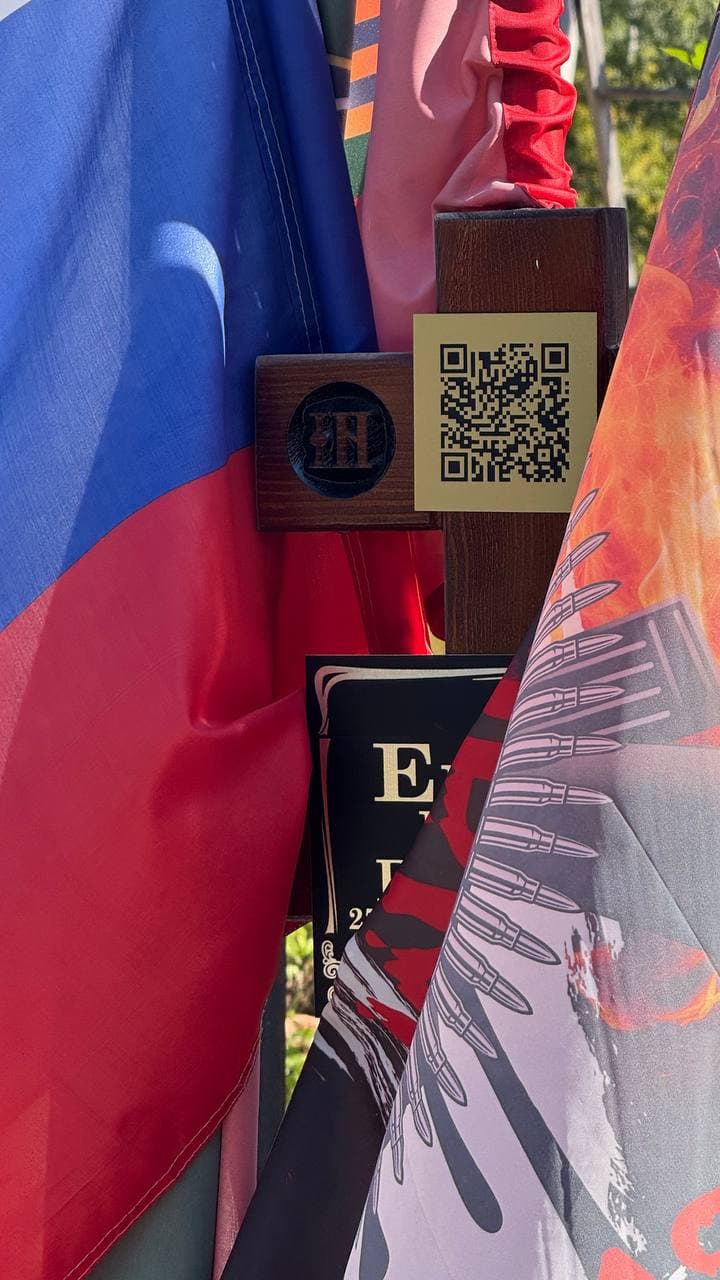 Золотистая табличка с QR‑кодом на деревянном кресте у венков